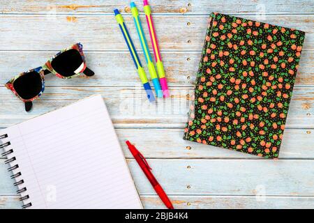 Draufsicht auf einen hölzernen Büroarbeitstisch mit Sonnenbrille, Markern, Stift und einem Notizbuch für die Arbeit Stockfoto