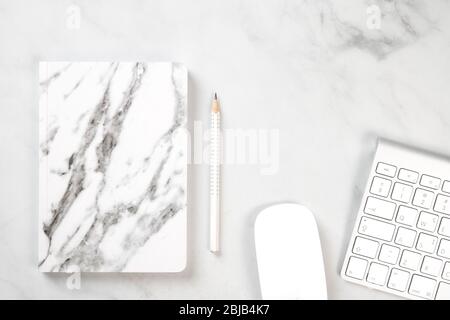 Weiße Schreibwaren auf einem weißen Marmorschreibtisch. Notizbuch aus Marmor, Tastatur, Maus und Bleistift. Arbeitsbereich Stockfoto