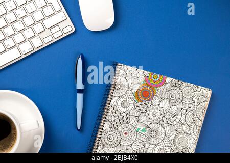 Blauer Schreibtisch mit Notebook, Stift, Tastatur, Maus und Kaffee. Konzept von oben Stockfoto