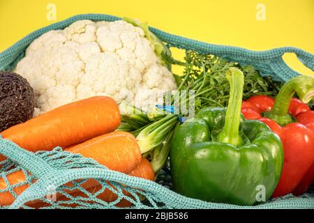 Nahaufnahme von frischem Gemüse in Netzbeutel, auf gelbem Hintergrund, bunte Zusammensetzung. Verschiedene Gemüse Anordnung, gesundes Essen Konzept. Stockfoto