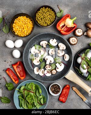 Rohe Pilze in einer Pfanne und Zutaten für das Kochen gesundes Frühstück auf einem grauen Hintergrund. Draufsicht. Stockfoto