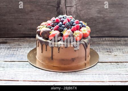 Schokoladenkuchen mit frischen Sommerbeeren. Dekoriert mit Erdbeeren, die in geschmolzene Schokolade getaucht sind. Stockfoto