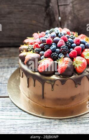 Schokoladenkuchen mit frischen Sommerbeeren. Dekoriert mit Erdbeeren, die in geschmolzene Schokolade getaucht sind. Stockfoto