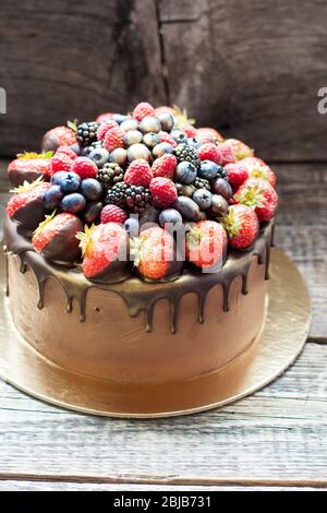 Schokoladenkuchen mit frischen Sommerbeeren. Dekoriert mit Erdbeeren, die in geschmolzene Schokolade getaucht sind. Stockfoto