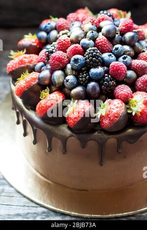 Schokoladenkuchen mit frischen Sommerbeeren. Dekoriert mit Erdbeeren, die in geschmolzene Schokolade getaucht sind. Stockfoto