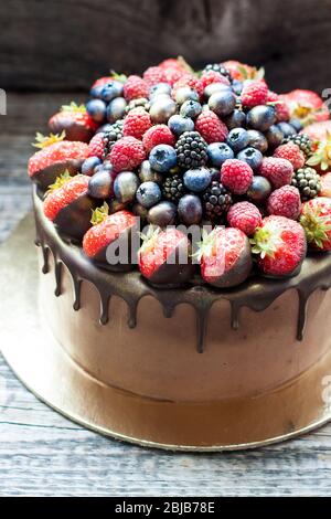 Schokoladenkuchen mit frischen Sommerbeeren. Dekoriert mit Erdbeeren, die in geschmolzene Schokolade getaucht sind. Stockfoto