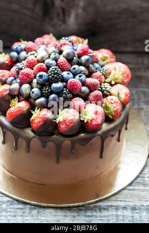 Schokoladenkuchen mit frischen Sommerbeeren. Dekoriert mit Erdbeeren, die in geschmolzene Schokolade getaucht sind. Stockfoto