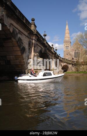 Flusskreuzfahrtschiff unter der englischen Brücke über den Fluss Severn in Shrewsbury mit Shrewsbury Abbey im Hintergrund. Stockfoto