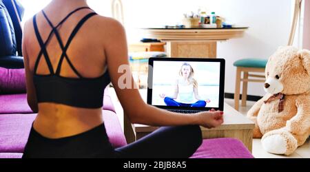 Rückansicht sportliche Frau in activewear sitzen auf Sofa mit gekreuzten Beinen Pose im Wohnzimmer tun Meditationspraxis verbessern innere Balance mit Internet und Note Stockfoto