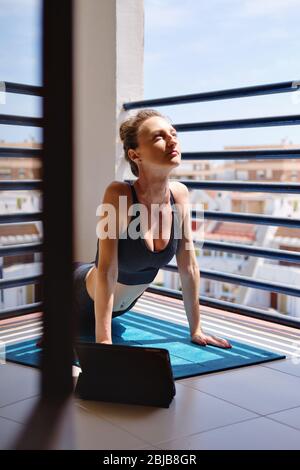 Frau tragen schwarze activewear Training im Sommer terrassenförmig zu Hause tun Yoga oder Pilates-Übung auf Matte. Nach oben schauenden Hund Pose Urdhva mukha shvanasan Stockfoto