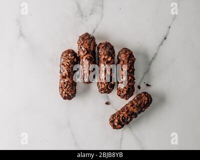 Set von hausgemachten Eclaren mit Schokolade auf Marmor Hintergrund. Draufsicht der köstlichen gesunden Profitroles mit Schokoladenglasur. Stockfoto