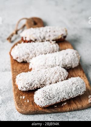 Hausgemachte eclairs mit Kokosnuss auf Holz Schneidebrett. Nahaufnahme der leckeren, gesunden profitroles mit geschredderten Kokosnuss. Kopieren Sie Platz für Text oder Design. Vertikale. Stockfoto