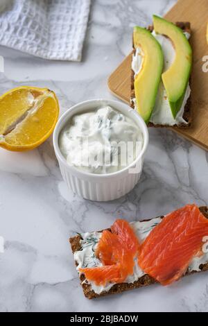 Frühstück am Morgen, zartes hausgemachtes Weichkäse auf Crackern mit geräucherter Forelle und Avocado Stockfoto