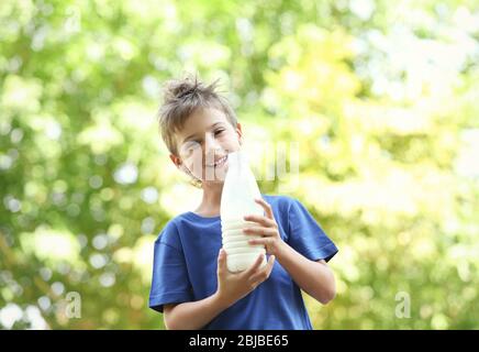 Fröhliches Kind in blauem Hemd hält Plastikflasche Milch auf verschwommenem Hintergrund Stockfoto