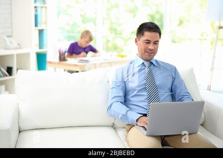 Vater arbeitet mit Laptop und sein Sohn Zeichnung auf Hintergrund Stockfoto