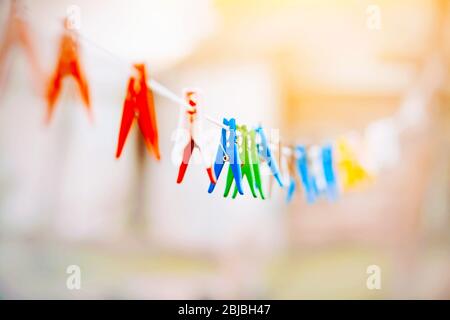 An einem hellen sonnigen Tag hängen bunte helle Wäscheklammern an einer langen weißen Wäscheleine und warten auf nasse Wäsche. Stockfoto
