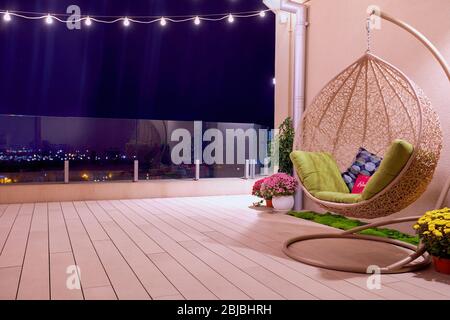 Dachterrasse mit hängendem Schaukelstuhl und Lichterkette in der Nacht Stockfoto