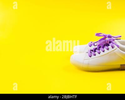 Weiße Sneaker mit lila Schnürung auf gelbem Hintergrund Stockfoto