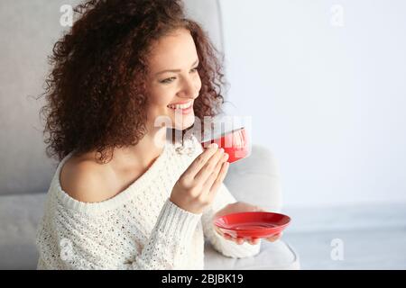 Junge attraktive Frau mit einer roten Tasse Kaffee und auf dem Sofa im Zimmer sitzen Stockfoto