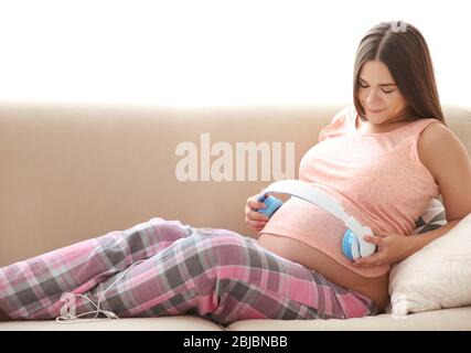 Schwangere Frau mit Kopfhörern auf Bauch Stockfoto