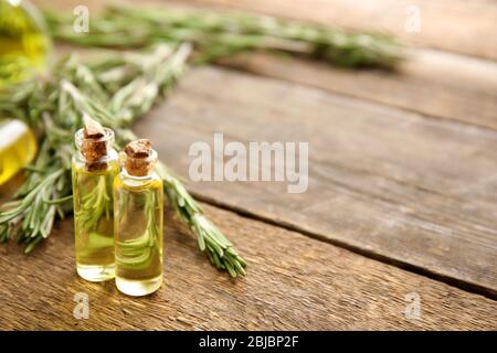Flaschen mit ätherischem Öl und Rosmarinzweigen auf Holzhintergrund, Nahaufnahme Stockfoto