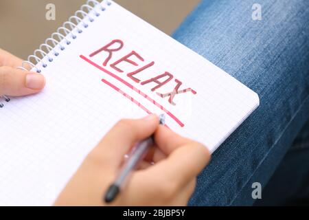 Junge Frau, die Wort 'Lax' in Notizbuch schreibt, liegt auf den Knien, Nahaufnahme Stockfoto