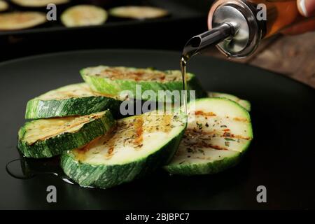 Weibliche Hand gießt Öl über Kürbisscheiben Stockfoto