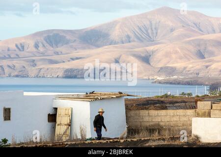 Eine einheimische Frau arbeitet vor ihrem Haus mit vulkanischer Landschaft im Hintergrund, Lanzarote, Kanarische Inseln, Spanien Stockfoto