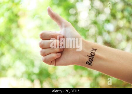 Weibliche Hand mit Tattoo Wort ENTSPANNEN, im Freien Stockfoto