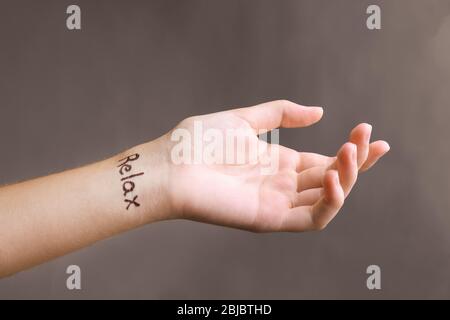 Weibliche Hand mit Tattoo Wort ENTSPANNEN auf grauem Hintergrund Stockfoto