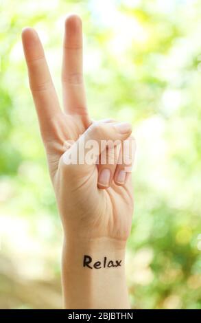 Weibliche Hand mit Tattoo Wort ENTSPANNEN, im Freien Stockfoto