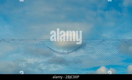 Wolke am blauen Himmel nahe der Gitterbarriere Stockfoto