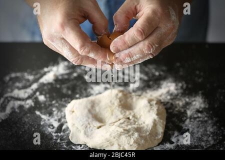 Männliche Hände, frisches Ei zum Teig auf dem Tisch hinzufügen Stockfoto