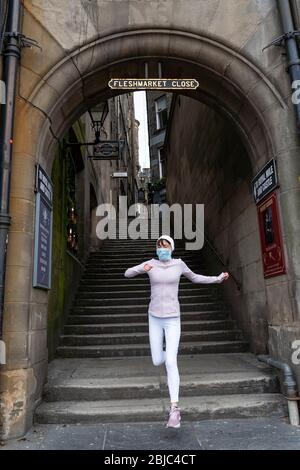 Edinburgh, Schottland, Großbritannien. 29. April 2020. Blick auf die Altstadt von Edinburgh, während die Sperrung des Coronavirus in Schottland fortgesetzt wird. Die Straßen bleiben verlassen und die Geschäfte und Restaurants geschlossen und viele vernagelt. Die schottische Regierung empfiehlt nun der Öffentlichkeit, Gesichtsmasken zu tragen. Weibliche Joggerin mit Gesichtsmaske läuft aus einem leeren Fleshmarkt Close. Iain Masterton/Alamy Live News Stockfoto