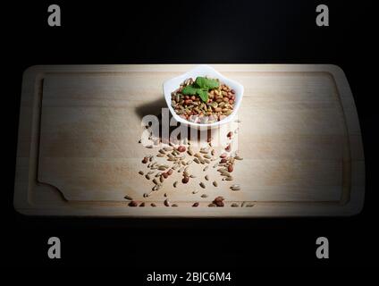 Bohnen und Roggen mit Minzblättern auf einer weißen Schüssel, auf einem Holzhackbrett, beleuchtet durch direktes Sonnenlicht Stockfoto