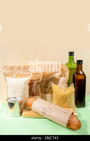 Vorrat von Lebensmitteln in Papier- und Zellophan-Verpackungen auf beige-grün. Müsli, Nudeln, Ölflaschen, Blechdose, Brot. Konzept Ohne Verschwendung. Kein Plastik. Stockfoto