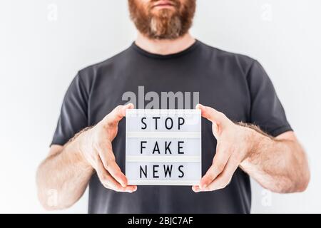 Fake News Infosemics during Covid-19 Pandemie Concept. Mann Hände halten Leuchtkasten mit Text Stoppen Fake News im Vordergrund. Die Leute wollen den Trut kennen Stockfoto