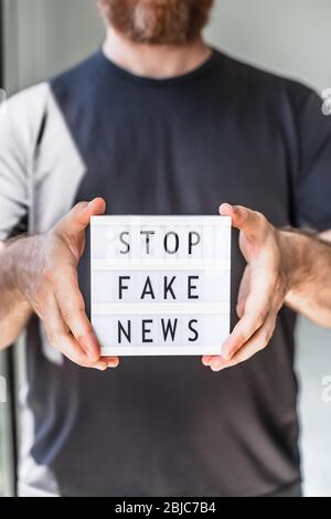 Fake News Infosemics during Covid-19 Pandemie Concept. Mann Hände halten Leuchtkasten mit Text Stoppen Fake News im Vordergrund. Die Leute wollen den Trut kennen Stockfoto