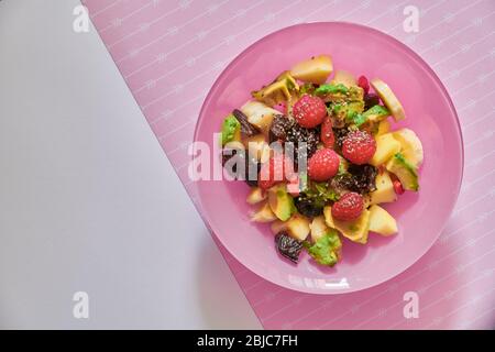 Frischer Obst veganer Salat in rosa Schale: Avocado, Himbeeren, Apfel, Banane, Pflaumen, Goji-Beeren und Chia-Samen Stockfoto
