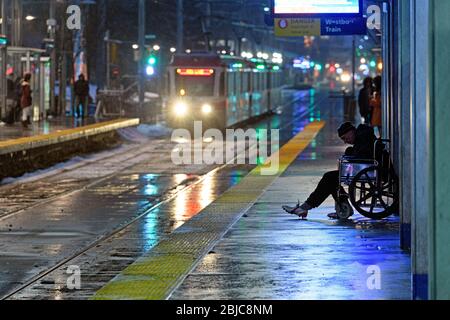 Ein Obdachloser in einem Rollstuhl auf einem Bahnsteig während einer regnerischen Nacht. Calgary, Alberta, Kanada Stockfoto