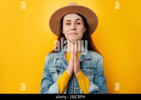Attraktive schöne junge Frau in Hut Hände in Gebet Geste mit Hoffnung, ziemlich nettes Mädchen bitten Hilfe und Unterstützung, Blick auf Kamera, trägt Stockfoto