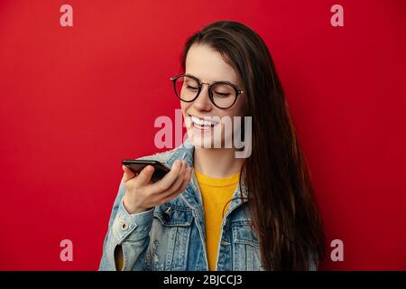 Lächelnde junge Frau in Brillen halten Telefon sprechen aktivieren virtuelle digitale Spracherkennung Assistent auf Smartphone, glückliche Mädchen Befehl Internet Stockfoto