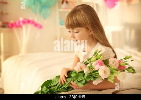 Nettes Geburtstagsmädchen sitzt auf dem Bett mit Blumenstrauß von schönen Blumen Stockfoto