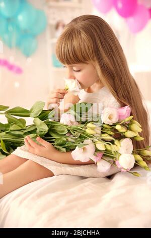 Nettes Geburtstagsmädchen sitzt auf dem Bett mit Blumenstrauß von schönen Blumen Stockfoto