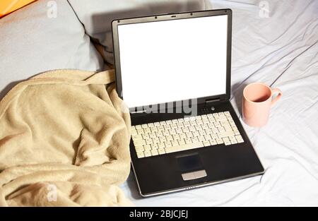 Laptop, bequeme Decke, Kissen und eine Tasse Tee auf einem nicht gemachten Bett in zerknitterte Bettwäsche komfortable Arbeitsplatz Arbeit von zu Hause, Home Entertainment Stockfoto