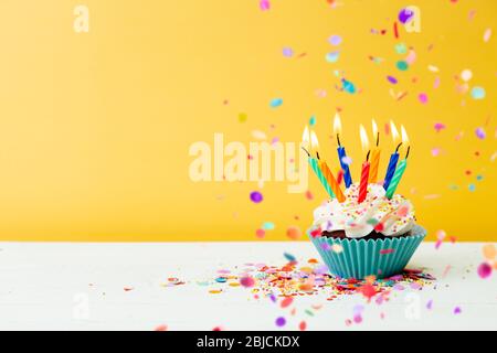 Ein farbenfroher Geburtstagskuchen mit sieben Kerzen und Konfetti auf gelbem Hintergrund Stockfoto