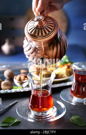 Weibliche Hand gießen türkischen Tee in traditionelles Glas auf dem Tisch Nahaufnahme Stockfoto