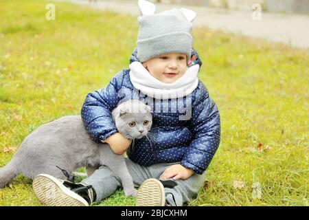 Liebenswert kleines Mädchen mit flauschigen Katze auf grünem Gras sitzen Stockfoto