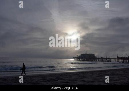 Extravagante Stimmung am Pier von Santa Monica, ein Paar auf dem Sand zu Fuß, im Hintergrund ein Sonnenuntergang durch einen bewölkten Himmel und ein ruhiges Meer mit Meer BU Stockfoto