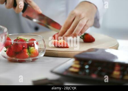 Kochkonzept. Professionelle Konditorei hacken Erdbeere auf Schneidebrett, Nahaufnahme Stockfoto